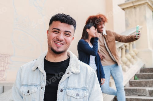 Preview: Front view of a young arab handsome man smiling and standing outdoors, at the background his two
