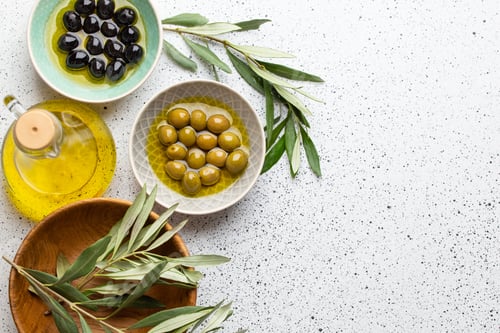 Preview: Green and black olives with olive oil in a glass bottle, olive tree sprigs and cut fresh ciabatta