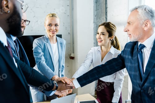 Preview: selective focus of cheerful multicultural businessmen and businesswomen putting hands together