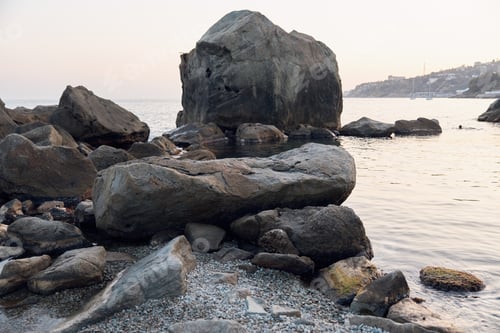 Preview: Tranquil lake scene with large rock surrounded by smaller rocks on the shore