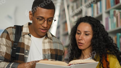 Preview: Two students African American man Arabian Latino woman together reading book textbook library