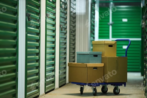 Preview: Stacked Cardboard Boxes on Dolly Cart Standing in Self Storage Facility Hallway