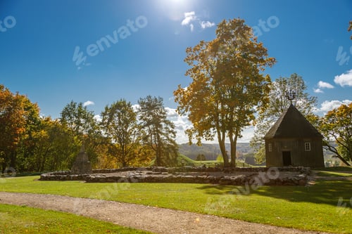 Preview: Sunlit autumn landscape in Kernave, Lithuania, featuring a historic wooden chapel