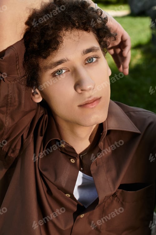 Preview: Curly-haired young man enjoying a sunny day in a vibrant green park setting