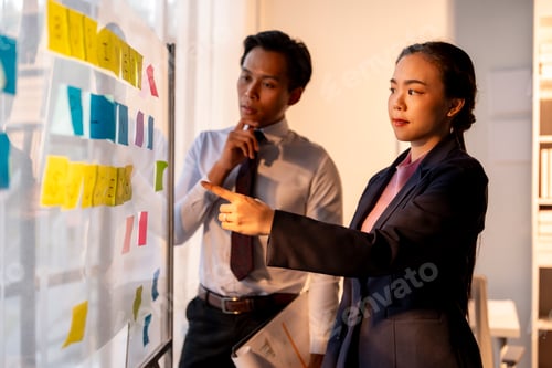 Preview: Two people are pointing at a white board with colorful sticky notes on it