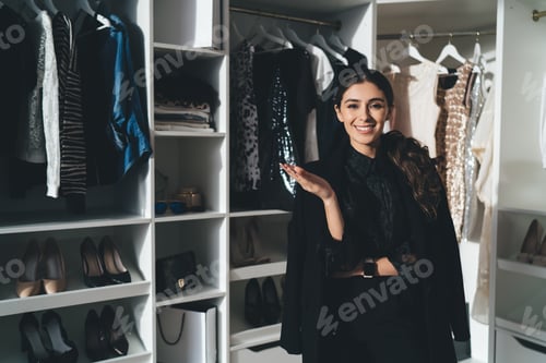 Preview: Smiling woman in elegant black outfit standing in wardrobe