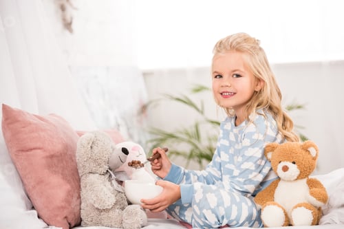 Preview: smiling child in pajamas feeding soft toys in bed