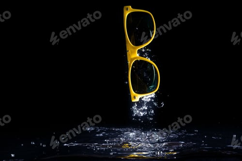 Preview: Yellow sunglasses splashing into water on black background. eyewear falling . Copy space.