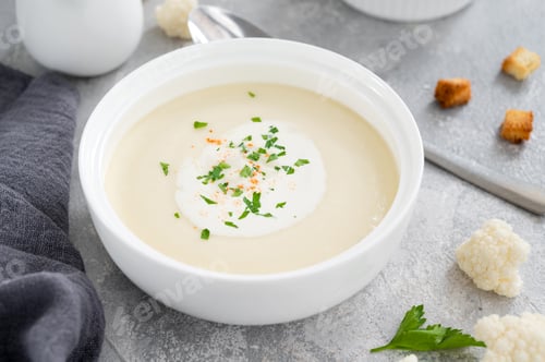Preview: Cauliflower soup puree in a white bowl with cheese, cream, spices and fresh parsley. Top view