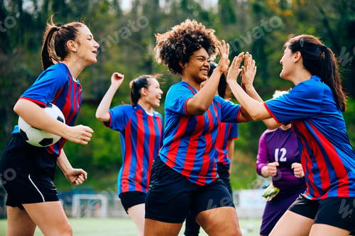 Preview: Happy female soccer players giving high-five after scoring a goal on a match.