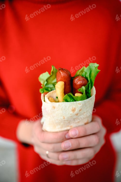Preview: the hands of a girl in red clothes are holding fast street food. shawarma is food in pita