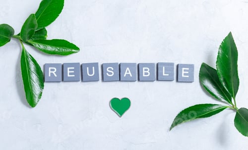 Preview: Word reusable made from wooden cubes, green leaves and green metal heart on background, horizontal