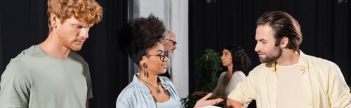 Preview: happy african american woman talking to bearded actor near interracial students in theater studio,