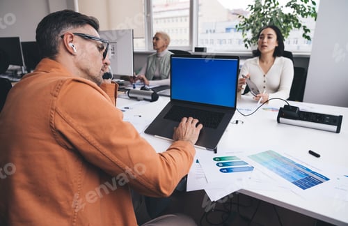 Preview: Man working on laptop at workplace against colleagues