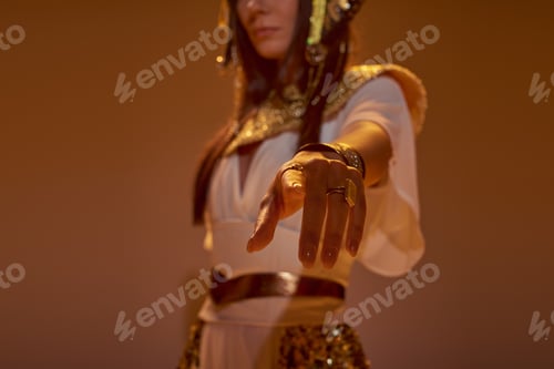 Preview: Cropped view of blurred woman in egyptian attire pointing with finger at camera on brown background
