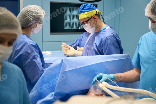 Preview: Surgeon in a yellow-blue cap takes an instrument from assistant