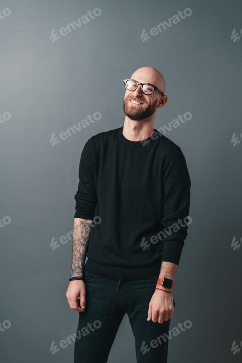 Preview: Young smiling man with beard and glasses on gray studio background