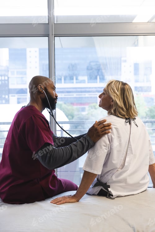 Preview: African american male doctor examining senior female caucasian patient using stethoscope at hospital