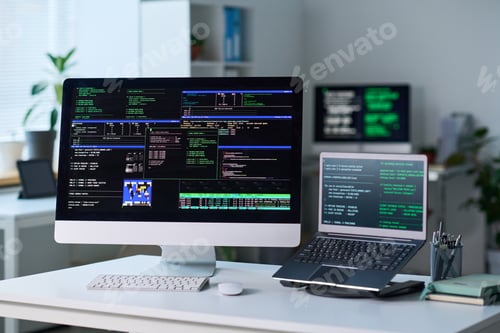 Preview: Office Desk Featuring Computer and Laptop Displaying Programming Code
