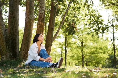 Preview: Portrait of asian girl relaxing, leaning on tree and resting in park under shade, smiling and