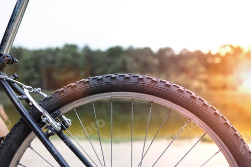 Preview: Closeup of the rear wheel of a mountain bike on the background of the river in summer at sunset.