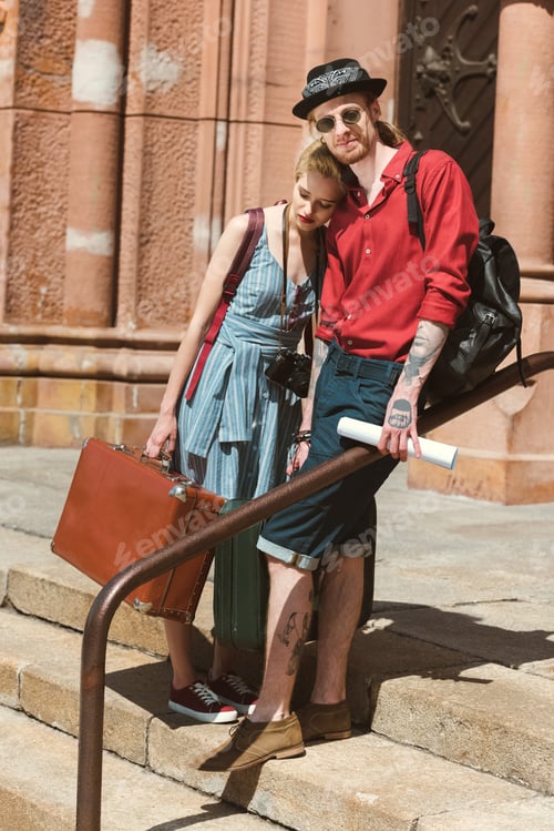 Preview: beautiful couple of tourists with vintage travel bags hugging in city