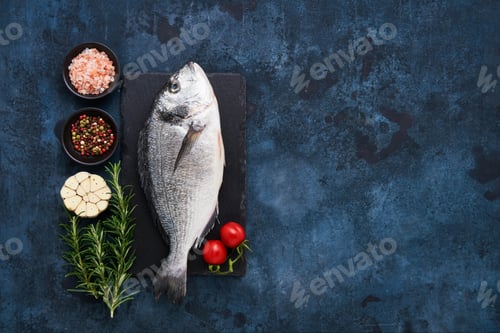 Preview: Raw dorado fish with spices on a dark blue background. Mediterranean seafood concept.