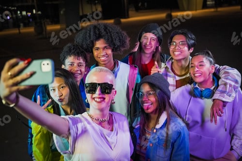 Preview: Group of young people with modern outfits taking a selfie in the street wth neon lights at night.