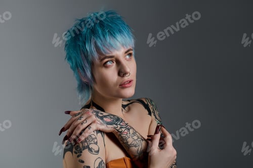Preview: Young woman with vibrant blue hair and stylish tattoos exudes confidence in studio setting