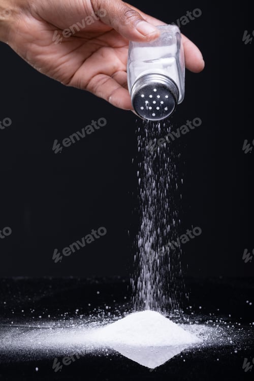 Preview: Cropped hand of african american man sprinkling salt with shaker against black background copy space