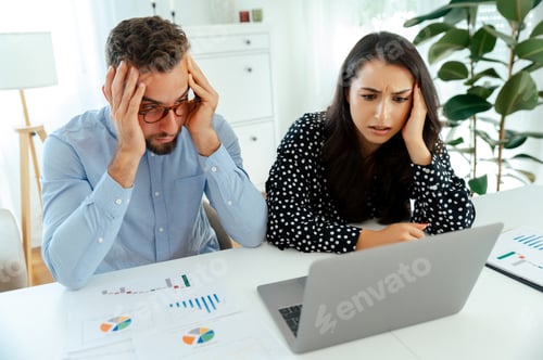 Preview: Stressed colleagues analyzing data and charts on a laptop and printed sheets at a desk, working