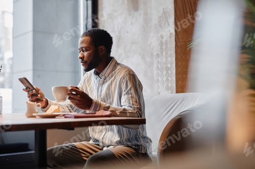 Preview: Side view of young African American man watching online video in mobile phone