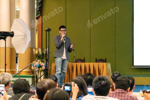 Preview: Closeup portrait of asian Speaker with casual suit on the stage over the presentation screen