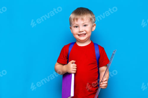 Preview: small happy smiling boy with glasses on his head, book in hands, schoolbag on his shoulders. back to