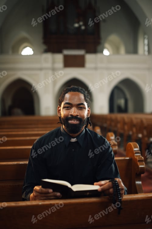 Preview: Young priest sitting in church pew reading the bible