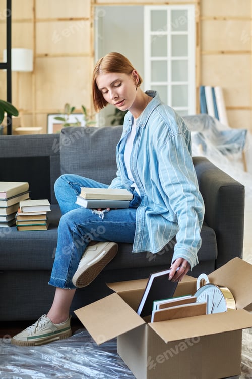 Preview: Young woman in casualwear taking book out of cardboard box