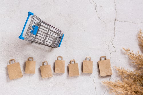 Preview: Kraft paper shopping bags in a row and a shopping cart on a concrete background. Top view.