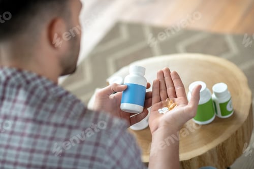 Preview: Young man in a checkered shirt hoding pills