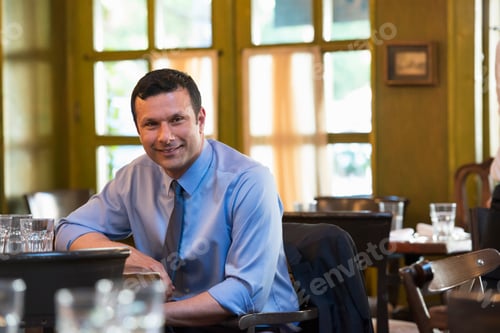 Preview: Business people outdoors. A latino man sitting at a table alone, relaxing.