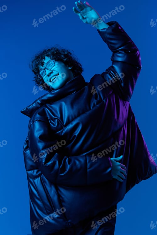 Preview: Man in winter jacket model poses and dances, hipster lifestyle, portrait blue background, mixed neon