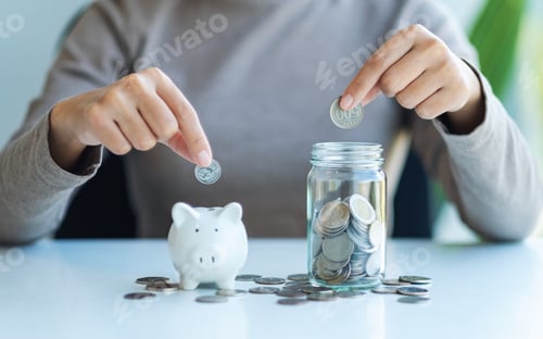 Preview: Closeup image of a woman putting coin into piggy bank and a glass jar for saving money concept