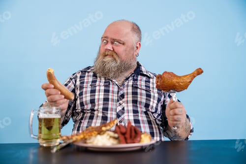 Preview: Doudting plus size man looks at sausage sitting at table with different fat food in studio