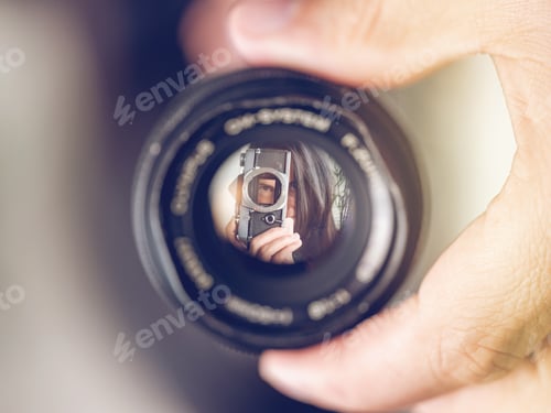 Preview: Lens with reflection of woman with analog photo camera