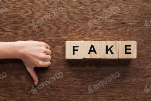Preview: cropped image of journalist showing thumb down to wooden cubes with word fake at wooden table