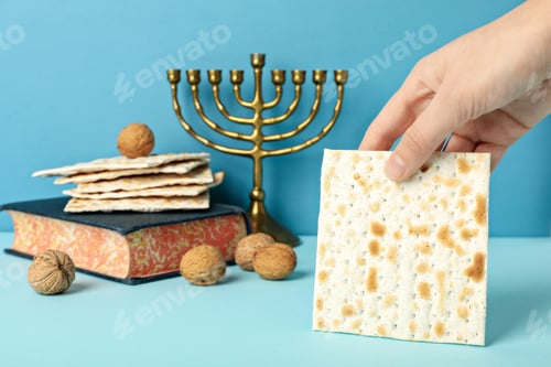 Preview: Matzo in hand, Torah, Hanukkiah and nuts on blue background