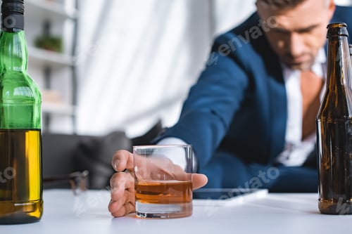 Preview: selective focus of glass with whiskey in hand of drunk businessman