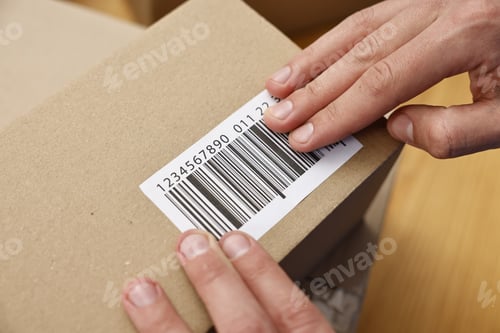 Preview: Man sticking barcode on parcel at table indoors, closeup