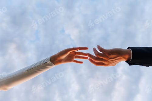 Preview: Hands of bride in white dress and groom in suit reaching each other, touching fingers on blue sky b
