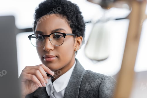Preview: portrait of african american businesswoman in grey blazer and eyeglasses holding hand near face