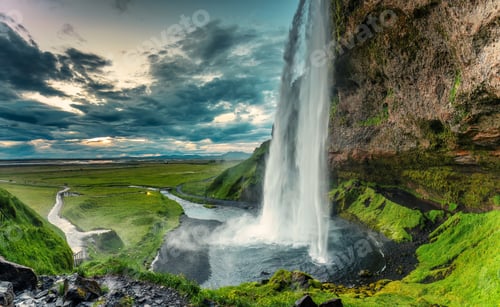 Preview: Beautiful Seljalandsfoss waterfall flowing and lush field on gloomy day in summer